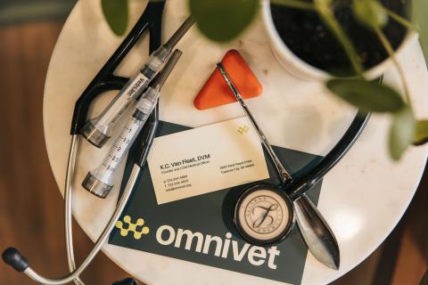 Dr. KC Van Fleet's business card alongside a stethoscope, syringes, and reflex hammer, symbolizing the expert care provided at Omnivet, a trusted emergency and urgent care veterinary clinic in Traverse City.